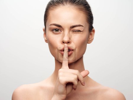 Attractive young woman making hush hush gesture with finger on lips, posing gracefully