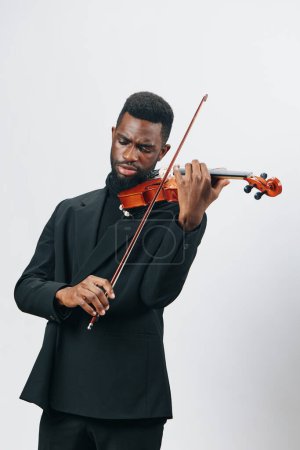 Eleganter afroamerikanischer Geiger im schwarzen Anzug, der auf weißem Hintergrund mit Geige performt