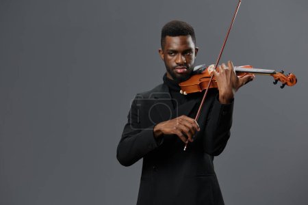 Photo for African American man in black suit playing violin on gray background in elegant musical performance portrait - Royalty Free Image