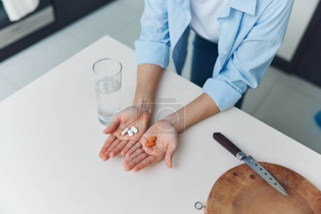 Frau hält Tabletten und Messer neben einem Glas Wasser auf weißem Tisch