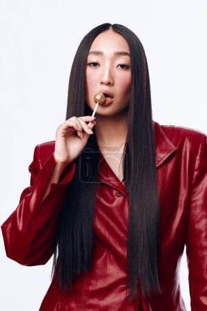 Foto de Mujer asiática con pelo negro largo en chaqueta de cuero rojo fumar cigarrillo en ambiente urbano - Imagen libre de derechos