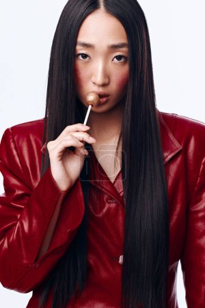 Foto de Mujer elegante con pelo largo y negro y chaqueta de cuero rojo fumando un cigarrillo en el fondo urbano - Imagen libre de derechos