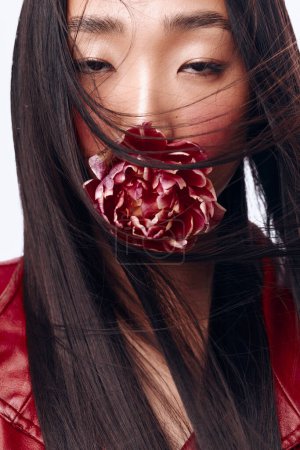 Téléchargez les photos : Belle femme aux longs cheveux noirs, soufflant dans le vent, tenant une fleur dans sa bouche - en image libre de droit