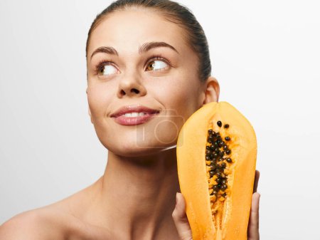 Téléchargez les photos : Portrait d'une femme tenant de la papaye fraîche et regardant la caméra à la lumière naturelle - en image libre de droit