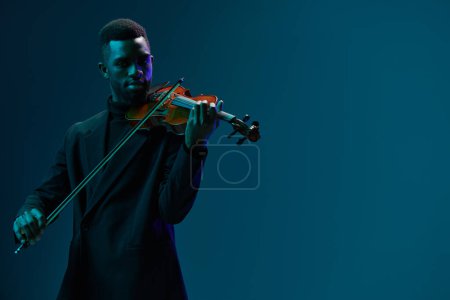 Foto de Elegante hombre afroamericano en traje negro tocando el violín sobre fondo azul en una actuación musical - Imagen libre de derechos