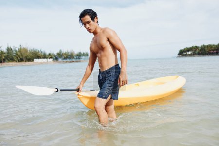 Téléchargez les photos : Serene Summer Vibes : Homme Asiatique faisant du kayak sur la plage tropicale, profitant de vacances saines et actives - en image libre de droit