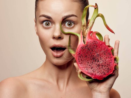 Photo for Woman fascinated by exotic dragon fruit, holding it in front of her face with eyes wide open - Royalty Free Image