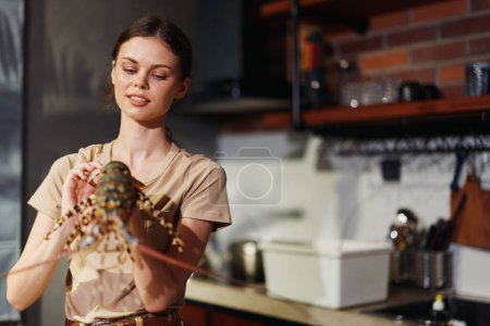 Una mujer sosteniendo una langosta frente a una cocina en un concepto de cocina de mariscos