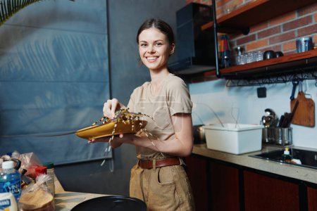 Foto de Mujer feliz sosteniendo caja de regalo de oro en la cocina, sonriendo brillantemente, expresando gratitud y alegría - Imagen libre de derechos