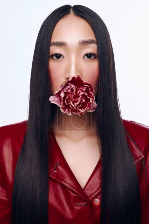 Photo for Beautiful woman with long black hair wearing a red jacket and flower in mouth poses for the camera - Royalty Free Image