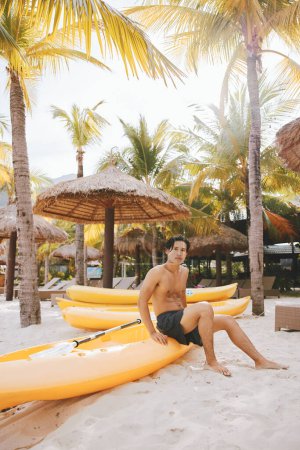 Téléchargez les photos : Kayak Adventure : Un homme asiatique heureux profitant des sports nautiques sur une plage tropicale - en image libre de droit