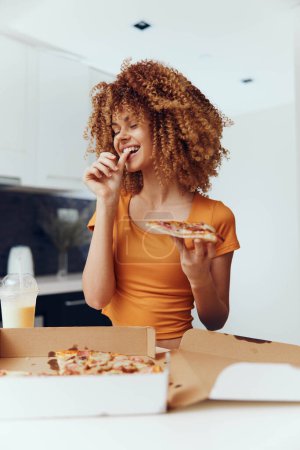 Photo for Young woman with curly hair enjoying a slice of pizza in front of a opened pizza box - Royalty Free Image