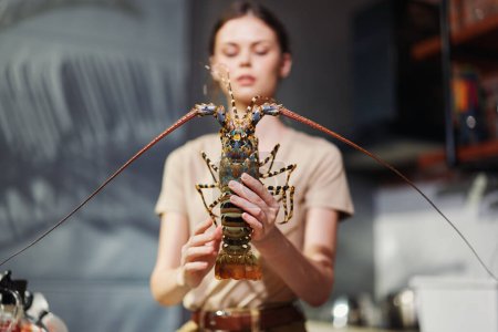 Téléchargez les photos : Femme tenant un homard à la main devant une cuisine - en image libre de droit