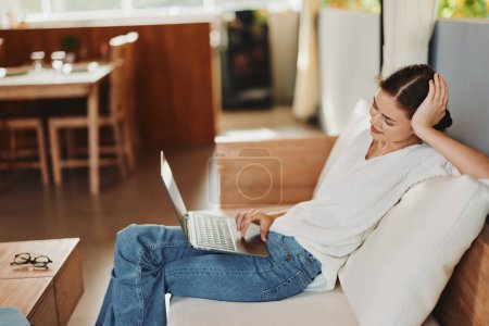 Photo for Woman Relaxing on a Cozy Sofa, Enjoying a Carefree Weekend at Home She is Sitting in a Modern Living Room, Smiling and Chatting Online while Shopping The Room is Contemporary and Comfortable, with a - Royalty Free Image