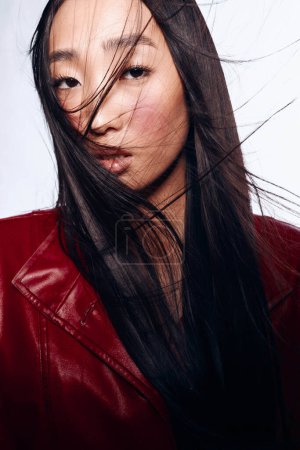Foto de Mujer con estilo en chaqueta de cuero rojo posando para la cámara con el pelo largo y negro - Imagen libre de derechos