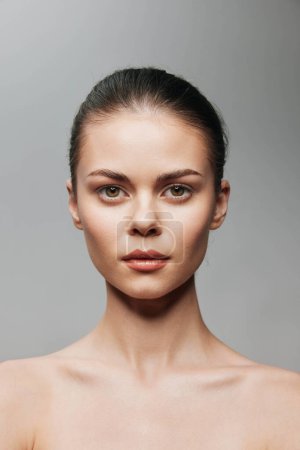 Natürliche Schönheit Porträt einer jungen Frau mit nacktem Gesicht sieht elegant und selbstbewusst auf grauem Hintergrund