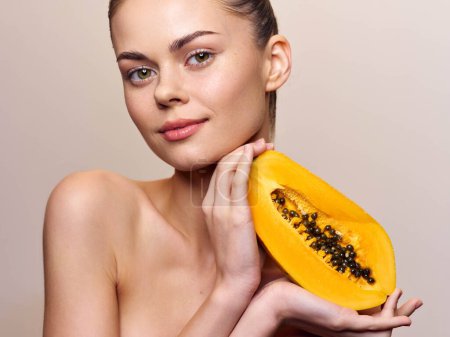 Téléchargez les photos : Jolie jeune femme posant avec des fruits de papaye sur son épaule, isolée sur fond beige, concept de mode de vie sain - en image libre de droit