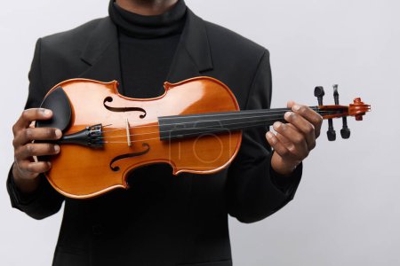 Elegant musician in black suit holding a violin against a white background, classical music concept