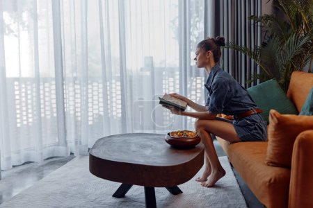 Cozy reading nook on orange couch by window with woman relaxing and enjoying a book at home