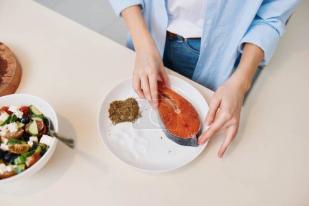 Foto de Mujer preparando comida saludable con salmón y ensalada en un plato en casa - Imagen libre de derechos