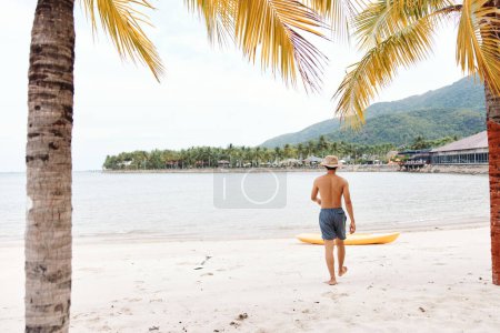 Glücklicher Asiate beim Kajakfahren am tropischen Strand mit dem bunten Kanu: Aktive Freizeit und Genuss im sonnigen Sommerurlaub