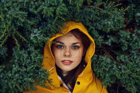 Femme en imperméable jaune entourée d'arbres verts dans un paysage forestier tranquille pendant une journée pluvieuse