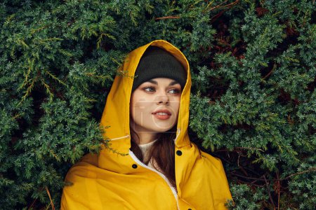 A woman in a yellow raincoat exploring the serene beauty of an evergreen forest during a nature trip