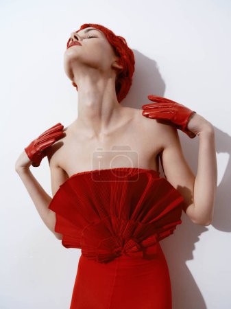 Photo for Elegant woman in a red dress and gloves posing with hands on head against white wall - Royalty Free Image