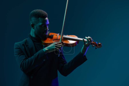 Foto de Hombre de traje tocando el violín con una iluminación dramática sobre un fondo oscuro creando una atmósfera de actuación musical cautivadora - Imagen libre de derechos