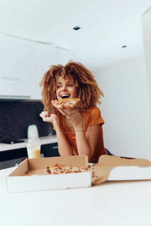 Photo for Woman enjoying a slice of pizza at a table in front of a box of pizza on a sunny day - Royalty Free Image