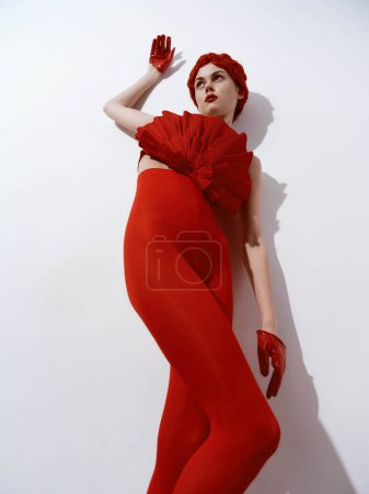 Elegant woman in red dress and gloves posing confidently against white wall, hands on hips