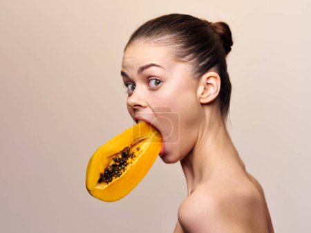 Woman biting into a ripe papaya fruit with a bite taken out, showcasing fresh and healthy tropical snack