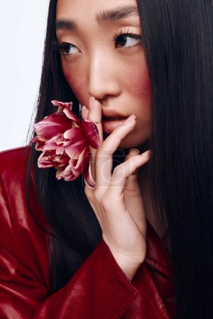 Woman with long black hair and red jacket holding a flower in front of her face in natural light portrait