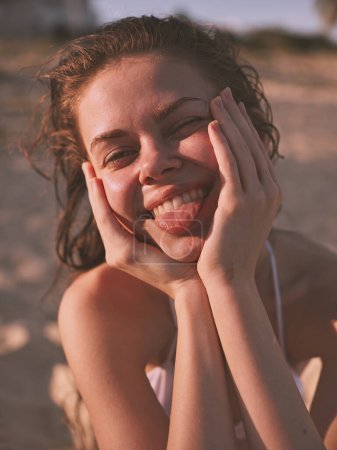 Foto de Mujer feliz con las manos en la cara sonriendo en la playa de arena durante el día soleado con el océano en el fondo - Imagen libre de derechos