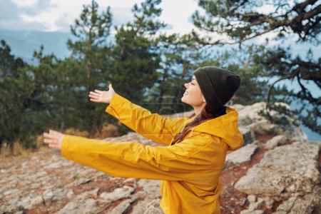 Téléchargez les photos : Femme en imperméable jaune bénéficiant de la vue magnifique depuis le sommet de la montagne avec les bras tendus - en image libre de droit