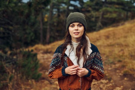 Una joven con un elegante sombrero y chaqueta de pie en un sendero forestal, abrazando la naturaleza y la aventura