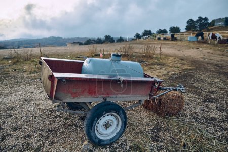 Foto de Carro rojo rústico con tanque industrial en el tranquilo entorno de campo, viajes de campo y concepto de negocios - Imagen libre de derechos
