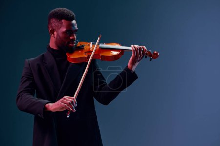 Foto de Hombre afroamericano conmovedor con traje negro tocando violín contra fondo oscuro - Imagen libre de derechos
