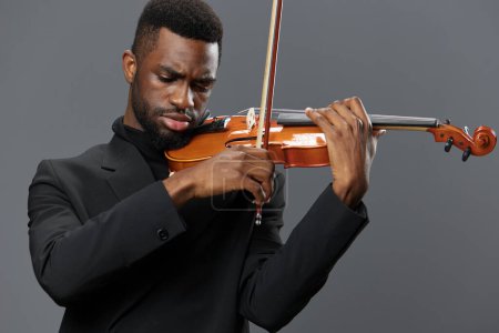 Foto de Elegante hombre afroamericano en traje negro tocando violín sobre fondo gris para música y concepto de performance - Imagen libre de derechos