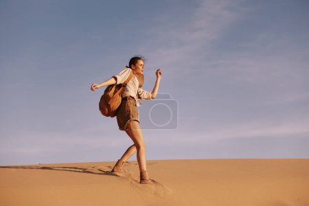 Woman trekking through the arid desert landscape with a backpack and hat under the scorching sun