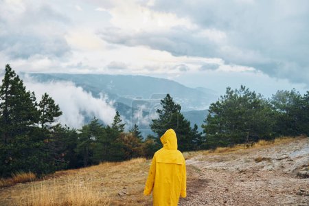 A person in a yellow raincoat standing on a dirt path with majestic mountains in the background on a travel adventure journeyrens