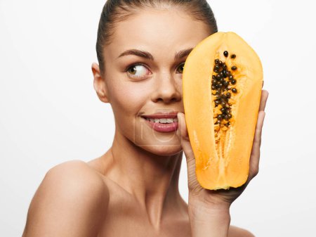 Téléchargez les photos : Portrait of a woman holding a ripe papaya in front of her face and looking at the camera - en image libre de droit