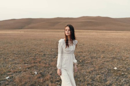 Téléchargez les photos : Femme en robe blanche debout en plein champ dans le désert, embrassant la liberté et la solitude - en image libre de droit