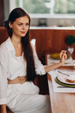 Téléchargez les photos : Woman enjoying a romantic dinner at home a beautiful brunette sits at a trendy dining table, smiling ecstatically as she indulges in a delicious homemade meal The room is adorned with elegant - en image libre de droit