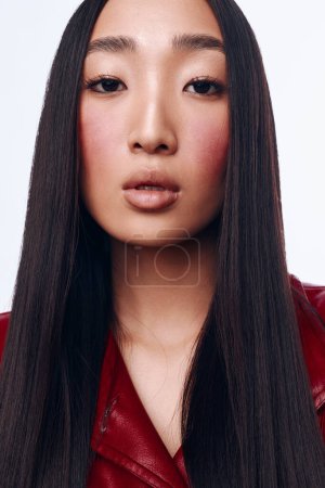 Foto de Joven mujer asiática con el pelo largo negro y chaqueta roja posando para la cámara en un entorno urbano con estilo - Imagen libre de derechos
