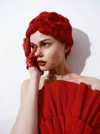 Geheimnisvolle Frau mit roten Haaren und passender Kleidung posiert Hand in Hand in dramatischem Modeporträt