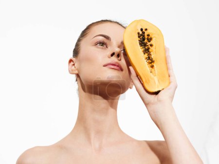 Téléchargez les photos : Woman holding a ripe papaya fruit and looking up at the camera in a sunny tropical setting - en image libre de droit