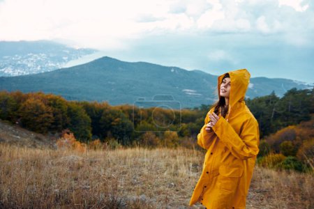 Woman in a yellow raincoat admiring majestic mountains while standing on a hill in peaceful solitude