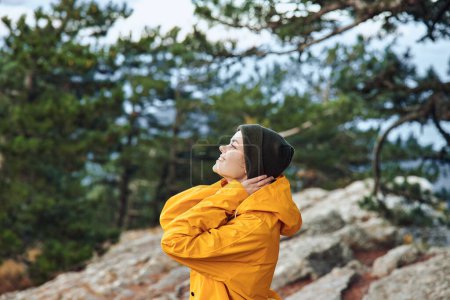 Photo for A woman in a yellow raincoat enjoying the breathtaking view from the top of a majestic mountain surrounded by trees - Royalty Free Image