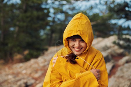 Photo for Smiling woman in yellow raincoat standing on rocky hillside enjoying outdoor adventure and travel experience, beauty of nature - Royalty Free Image